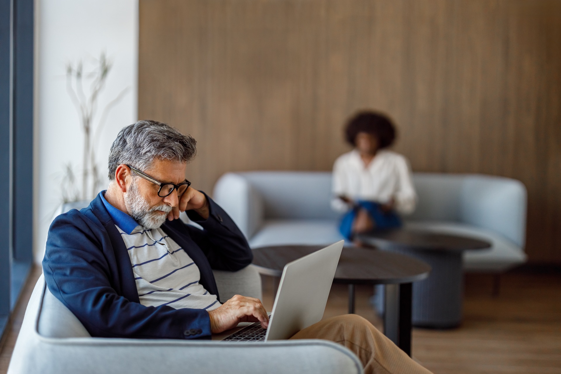 An older man with gray hair and glasses sits focused at a laptop in a modern shared workspace &mdash; a small business owner crafting his first welcome email sequence